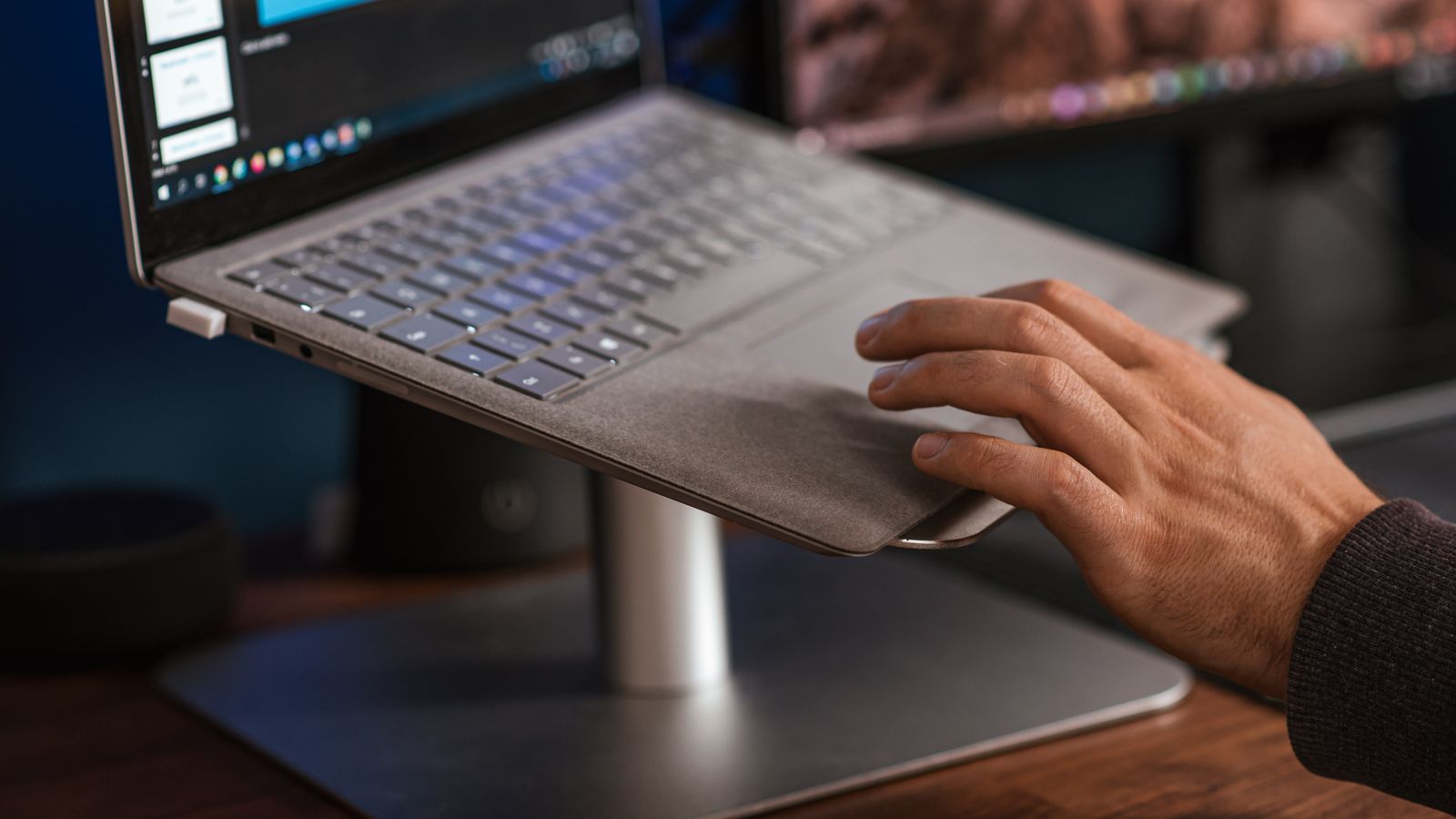 A hand using a laptop on a desk stand.