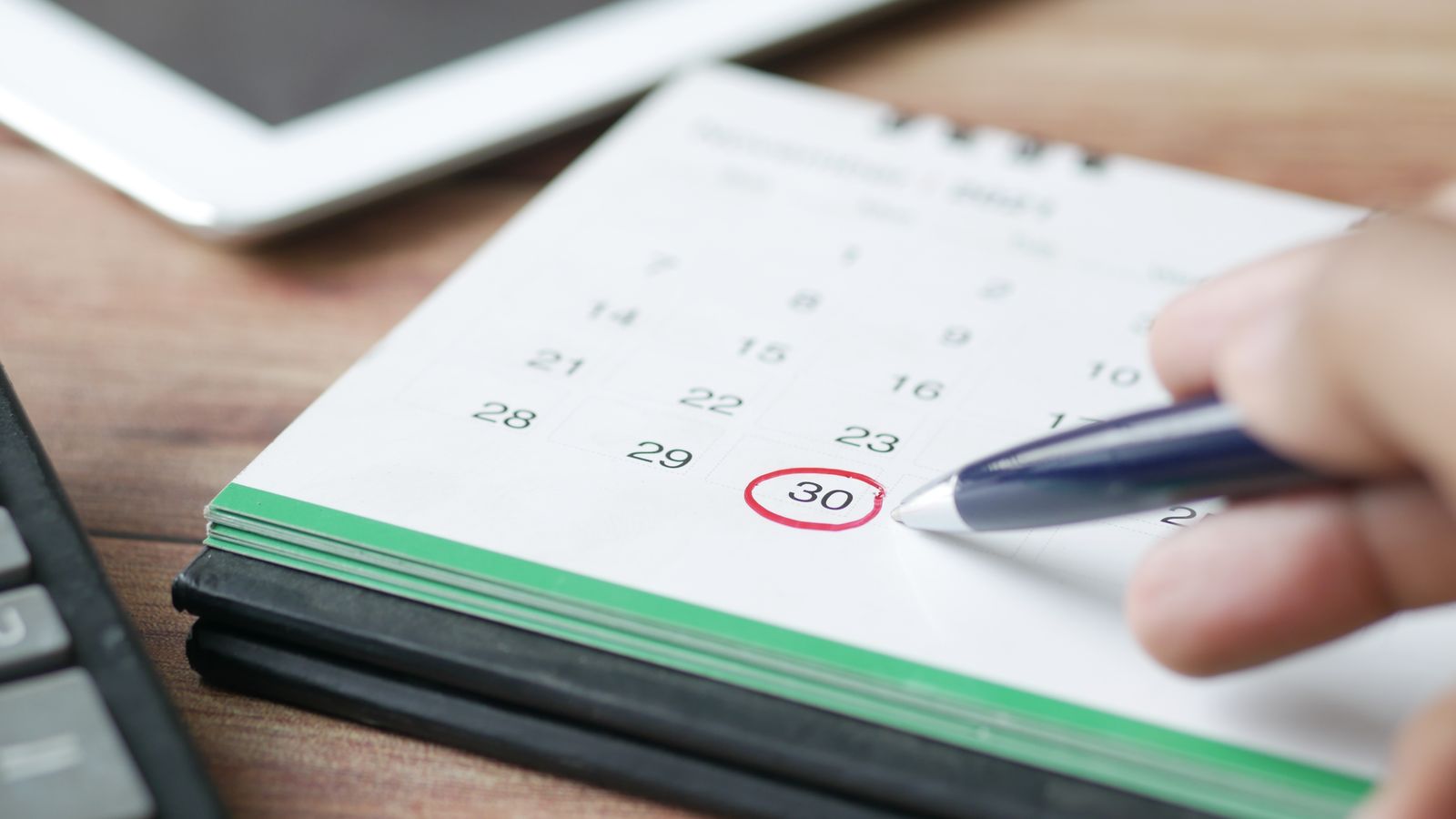 A hand pointing to a date on a paper calendar.