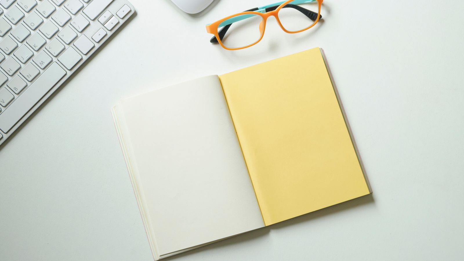 A notebook beside a keyboard and eyeglasses.