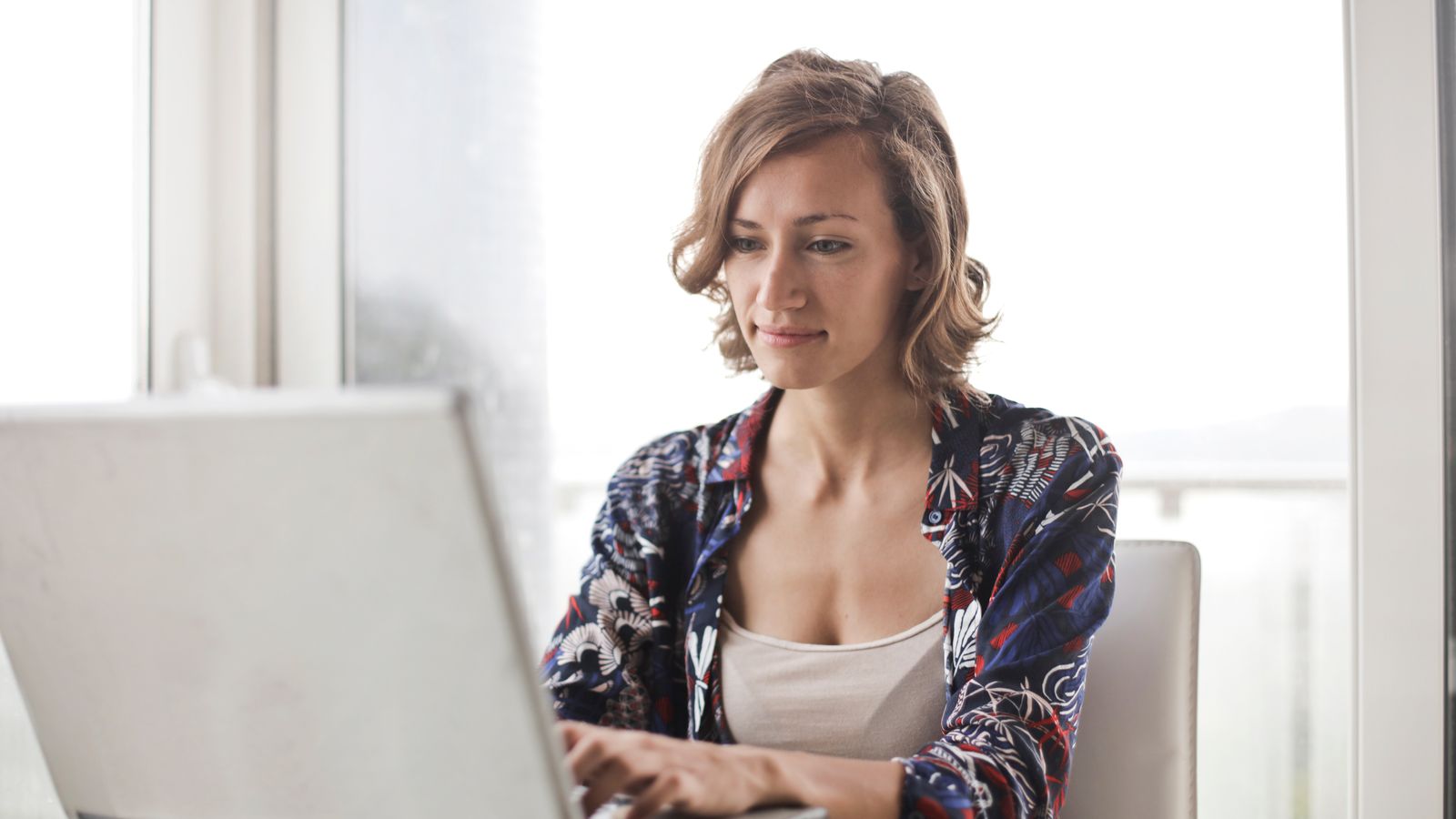 A woman typing on a laptop in a bright workspace.