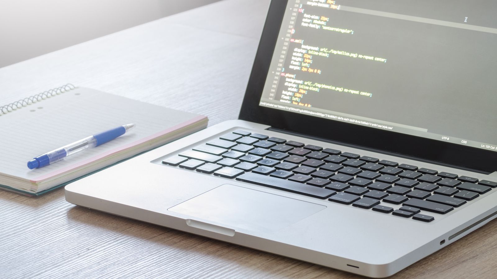A laptop showing code beside a notebook and pen.